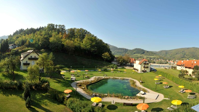 Residenz Wachau - Gartenanlage, © Hotel Donauterrasse Gartenanlage mit Teich, Liegestühlen und Sonnenschirmen, umgeben von Hügeln und Häusern.