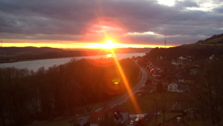 Sonnenuntergang1, © Gasthof Donaublick Sonnenuntergang über einer Landschaft mit Fluss und Straße.