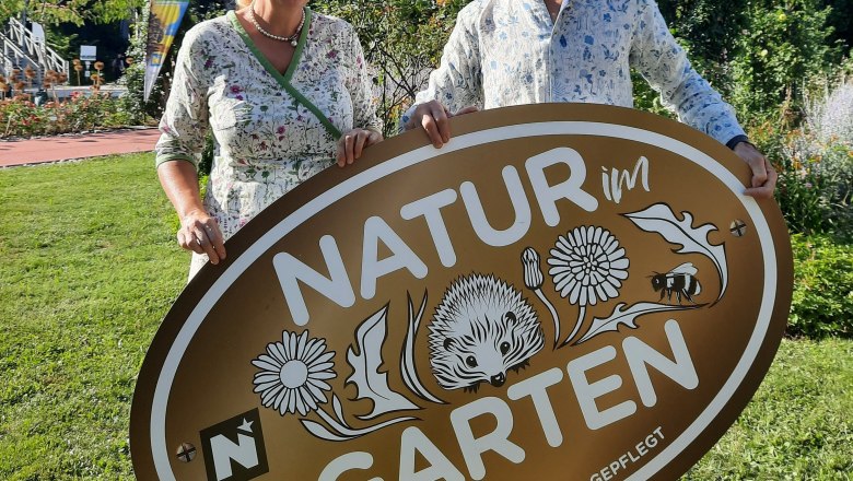 GrünTon Cottage, © Ingrid Kralovec Zwei Personen halten ein Schild mit der Aufschrift 'Natur im Garten'.