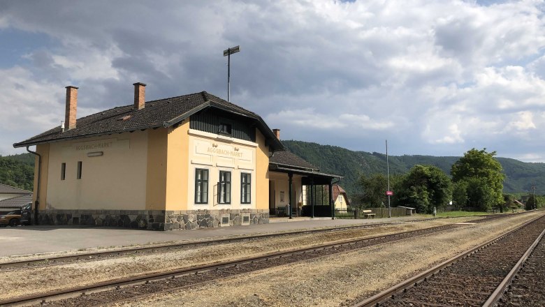 Bahnhof Aggsbach-Markt, © Donau NÖ Tourismus Bahnhof Aggsbach-Markt mit Gleisen und bewölktem Himmel.