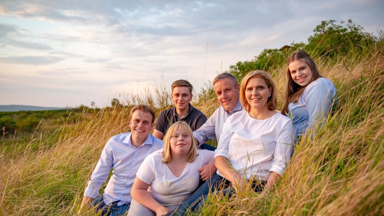 Familie Stift, © Martin Lifka Photography Eine Gruppe von sechs Personen sitzt in einem Feld bei Sonnenuntergang.