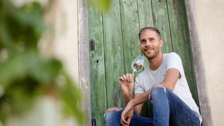 Bernhard Winter, © Astrid Bartl Ein Mann sitzt vor einer grünen Holztür und hält ein Weinglas in der Hand.