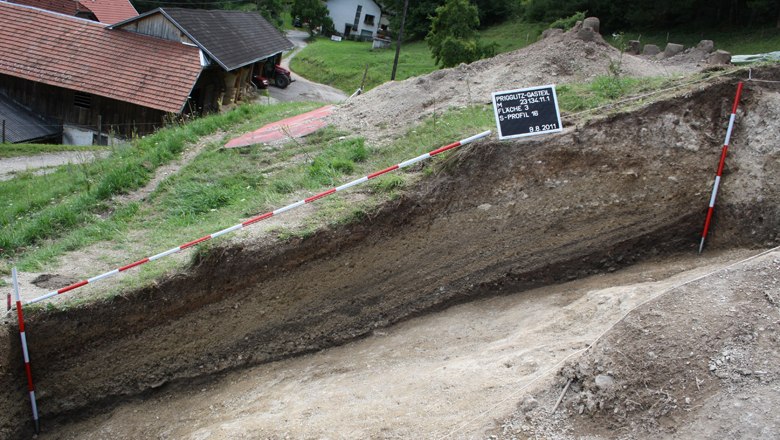Feine Schichten einer Erzaufbereitungshalde in der archäologischen Ausgrabung, © Landessammlungen Niederösterreich Ausgrabung mit sichtbaren Erdschichten und Messlatten.