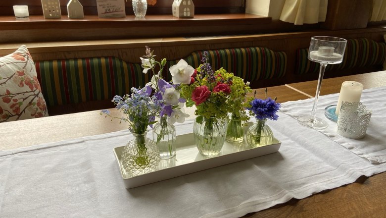 Tische schön dekoriert, © Wiener Alpen Ein Tisch mit einer weißen Tischdecke, dekoriert mit kleinen Vasen voller bunter Blumen und Kerzenhaltern.