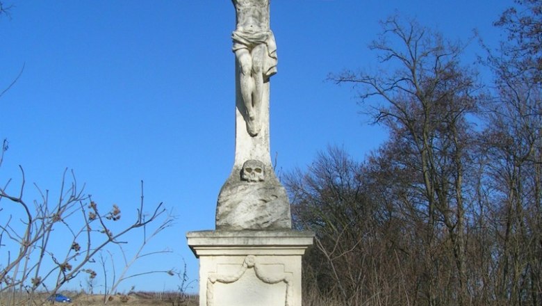 Vergessener Herrgott, © Gemeinde Retzbach Steinkreuz mit Jesusfigur in einer verwilderten Landschaft unter blauem Himmel.