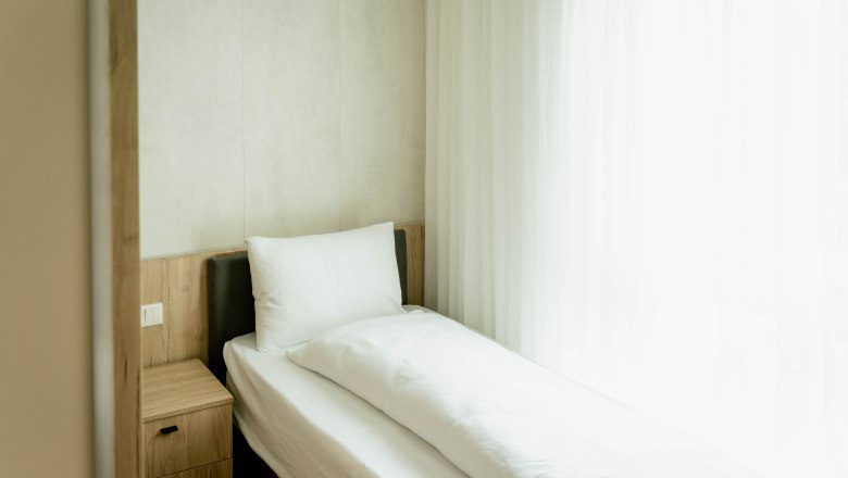 Hotel Lamede, © Hotel Lamede Einzelbett in einem hellen Hotelzimmer mit weißer Bettwäsche und einem Nachttisch.