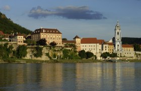 Aussenansicht Dürnstein und Schloss, © Hotel Schloss Dürnstein GmbH Außenansicht von Dürnstein mit Schloss und Kirche am Flussufer.