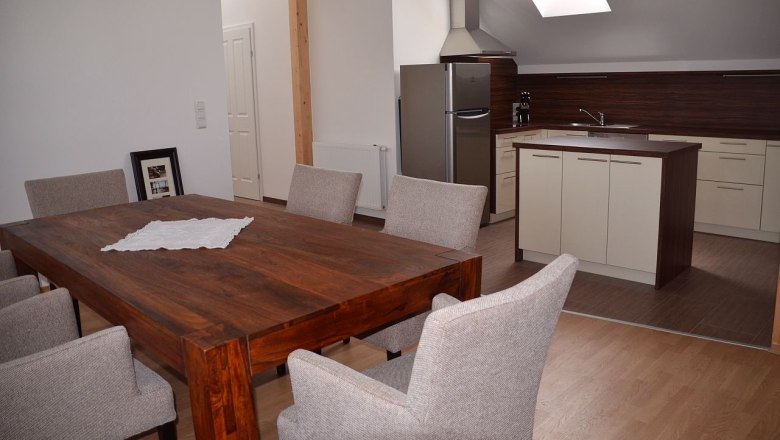 Esstisch, © Familie Herrmann Moderner Essbereich mit Holztisch und grauen Stühlen, angrenzend an eine Küche mit Insel und Dachfenster.