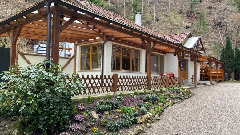 Die KlammWirtin - Hausansicht, © Wiener Alpen Ein Gasthaus mit Holzdach und Blumengarten vor einem bewaldeten Hang.