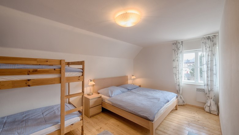 Top 6 - Schlafzimmer, © VP FeWo OG Helles Schlafzimmer mit Doppelbett und Etagenbett, Holzboden und Fenster mit Vorhängen.