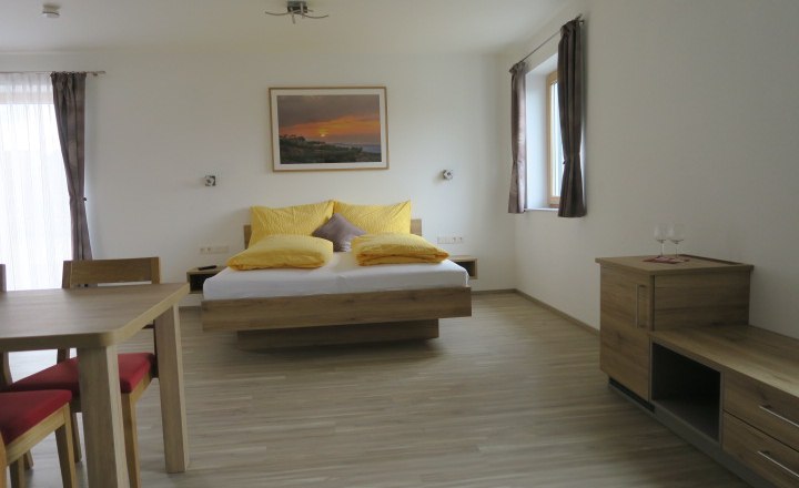 Gästezimmer neu, © Ettenauer Weine Modernes Gästezimmer mit Doppelbett, Holzmöbeln und gelben Kissen.