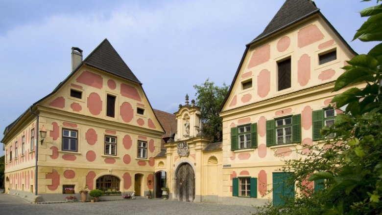 Hausansicht, © Weingut Holzapfel Historisches Gebäude mit verzierten Fassaden und Torbogen.