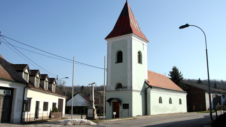 Guttenbrunn, © Gemeinde Ottenthal Kirche mit rotem Dach und Turm in einem Dorf bei klarem Himmel.