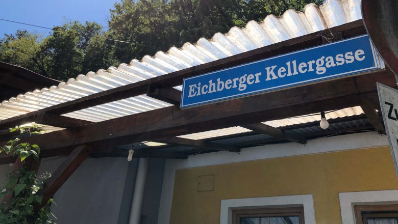 Eichberger Kellergasse, © Donau Niederösterreich Schild mit der Aufschrift 'Eichberger Kellergasse' an einem Gebäude mit Wellblechdach.