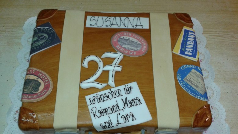 Tortenbäckerei, © Konditorei Köller Eine Torte in Form eines Koffers mit Aufklebern und der Zahl 27.