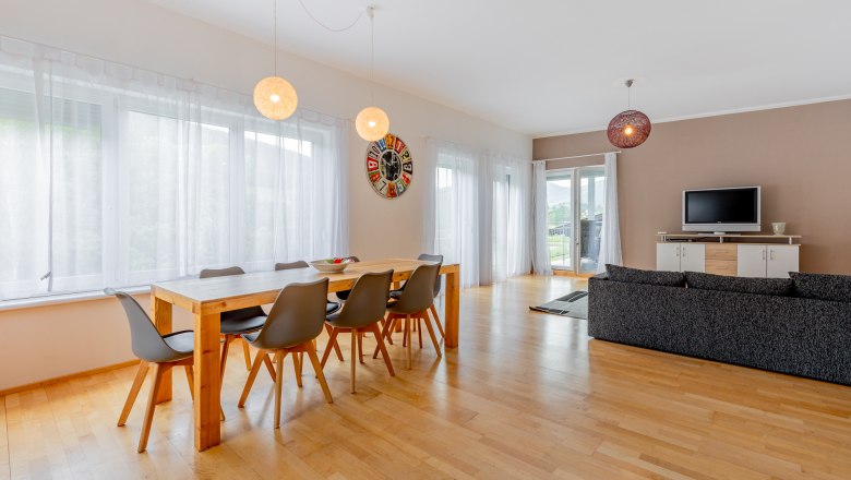 Essbereich, © Wiener Alpen / Christian Kremsl Moderner Essbereich mit Holztisch, grauen Stühlen und großer Fensterfront.