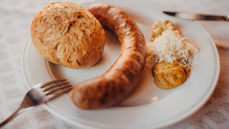 Braumeisterwürstel mit Biertrebernlaberl, © Niederösterreich Werbung/Daniela Führer Ein Teller mit einer Bratwurst, einem Brötchen, Senf und geriebenem Meerrettich.