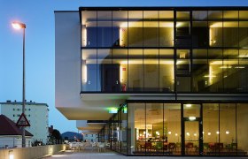 arte Hotel, © arte Hotel Modernes Hotelgebäude mit Glasfassade bei Dämmerung, beleuchtete Innenräume sichtbar.