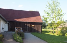 Pfarrzentrum-Stadl, © MG Sallingberg Ein Gebäude mit rotem Dach und Holzwänden, umgeben von grüner Landschaft und Bäumen.