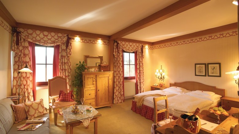 Zimmerbeispiel im Landhaus Bacher, © Landhaus Bacher Gemütliches Hotelzimmer im Landhausstil mit Doppelbett, Sofa, Tisch und rustikalen Holzmöbeln.