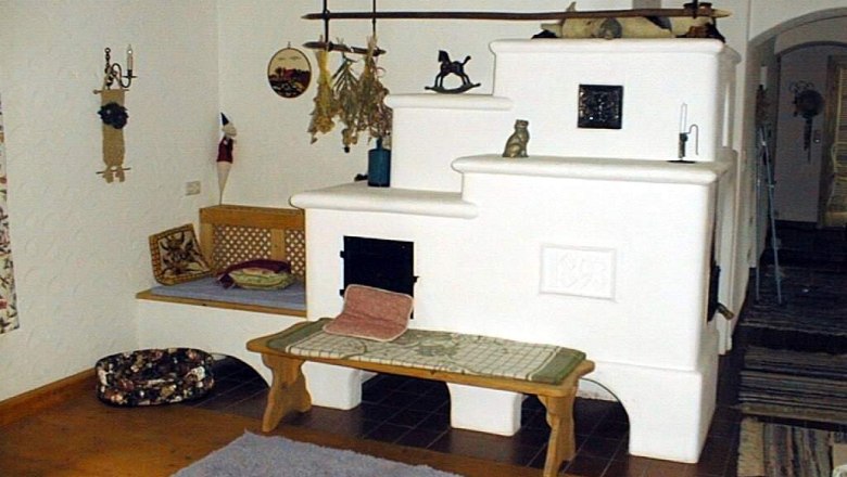 Kamin im Ferienhaus Goldegg, © Ferienhaus Koch Gemütlicher Raum mit weißem Kachelofen und Holzbalken.