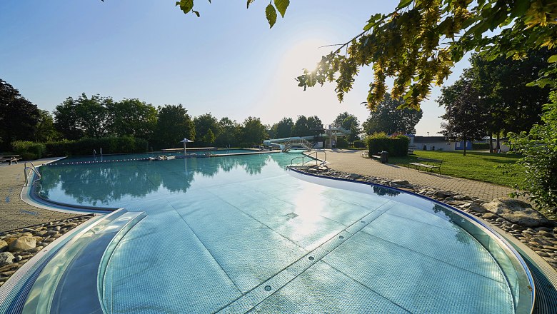 Freibad Absdorf, © Philipp Monihart Ein Freibad mit klarem Wasser, umgeben von Bäumen und einem sonnigen Himmel.