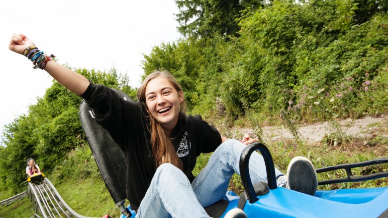 Eibl-Jet, © DorisSchwarzKoenig.at Eine lachende Person fährt auf einer Sommerrodelbahn, umgeben von grüner Natur.