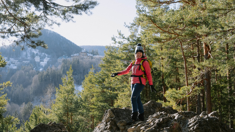 Kulturwandern zur Doppelreiterwarte, © Luxusgämsen Person in pinker Jacke wandert auf einem felsigen Pfad im Wald mit Bergen im Hintergrund.