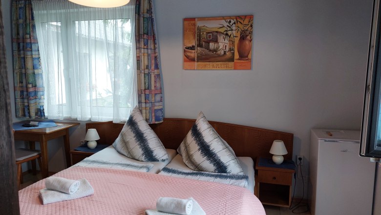 TDR-Pension Welserhof, © Bartfai Gemütliches Hotelzimmer mit Doppelbett, Nachttischlampen, kleinem Kühlschrank und Fenster mit Vorhängen.