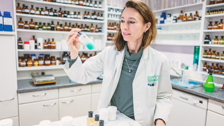 World of STYX- Labor, © Styx Naturkosmetic GmbH Eine Frau im weißen Laborkittel hält ein Reagenzglas mit blauer Flüssigkeit in einem Labor.