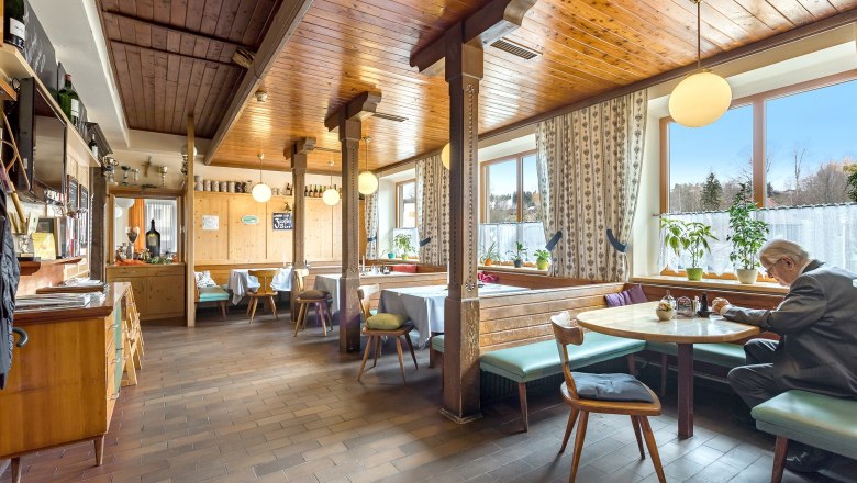 Waldviertler-Hof Gaststube, © Waldviertler-Hof Gemütliche Gaststube mit Holzmöbeln und großen Fenstern, ein Mann sitzt an einem Tisch.