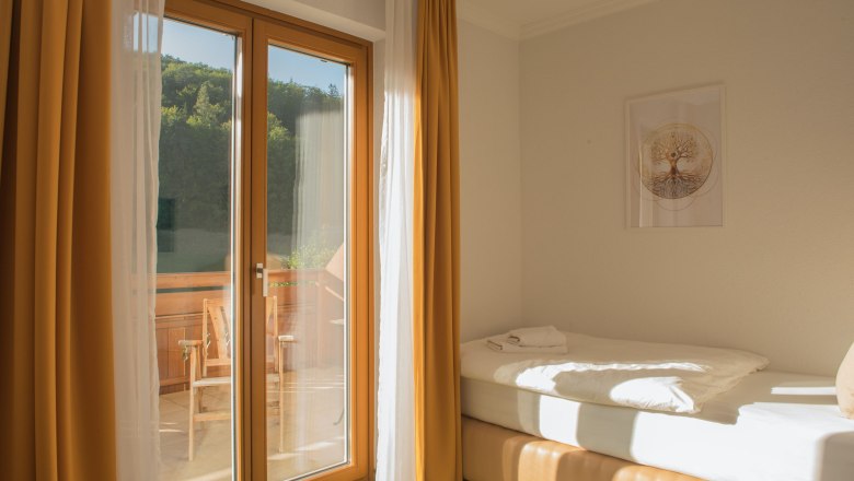 Einzelzimmer mit Balkon, © Dorfschmiede eG Einzelzimmer mit Balkon, Bett, gelbe Vorhänge, Holzbalkon, sonnig.