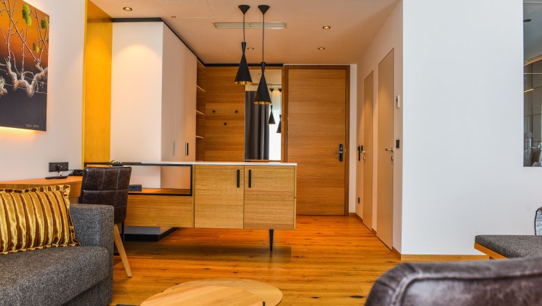 Suite Hotel Klinglhuber, © Franz Klinglhuber GmbH Innenansicht einer modernen Hotelsuite mit Holzboden, grauem Sofa und hölzernem Schreibtisch.