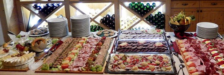 Schmankerl, © Fam. Böswirth Buffet mit verschiedenen Fleisch- und Käseplatten vor einem Weinregal.