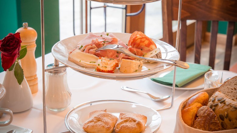 Frühstück, © Schlossschenke Ein Frühstückstisch mit einer Etagere voller Aufschnitt, Marmeladen und Brötchen, daneben ein Glas Orangensaft.