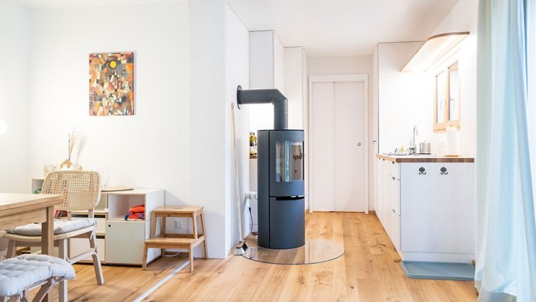 Innenbereich Luna, © WW Wohnwagon GmbH Moderner Wohnbereich mit Holzfußboden, Kaminofen, Esstisch und Küchenzeile.