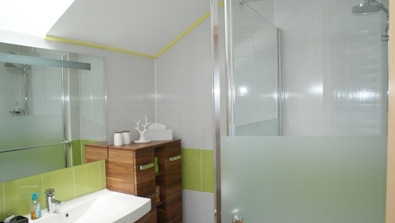 Badezimmer, © Familie Zwinz Modernes Badezimmer mit Waschbecken, Holzschrank und Dusche mit Glaswand.