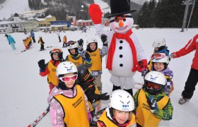 Happylift Semmering, © Josef Latzelsperger Kinder in Skiausrüstung posieren mit einem Schneemann auf einer Skipiste.