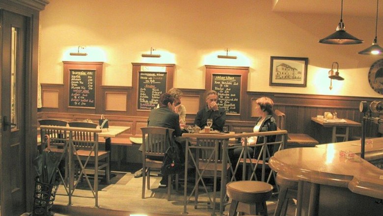 Braugasthof Adlerbräu, Innenansicht, © Braugasthof Adlerbräu Innenansicht eines gemütlichen Gasthauses mit Holzmöbeln und drei Personen an einem Tisch.