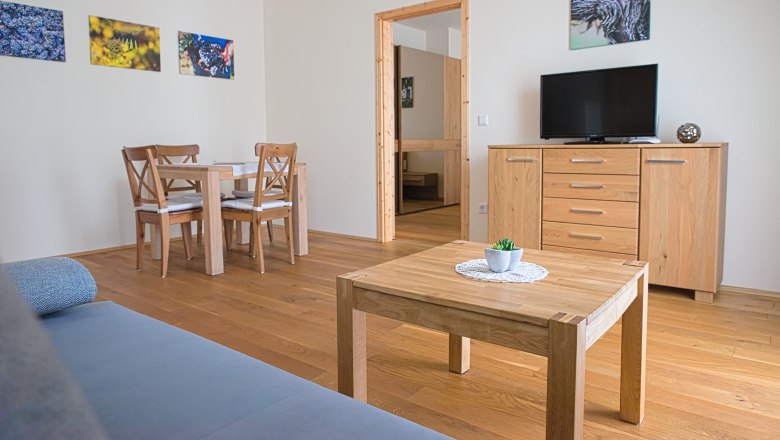 Gästezimmer, © Christoph Wurst Ein modernes Gästezimmer mit Holzmöbeln, einem Tisch, Stühlen, einem Fernseher und Wandbildern.