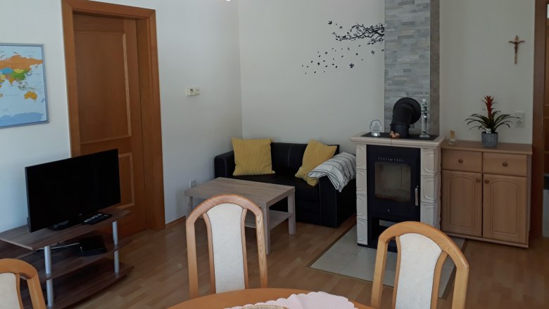 Wohnküche, © Barbara Muck Wohnzimmer mit Kamin, Sofa, Tisch und Fernseher.