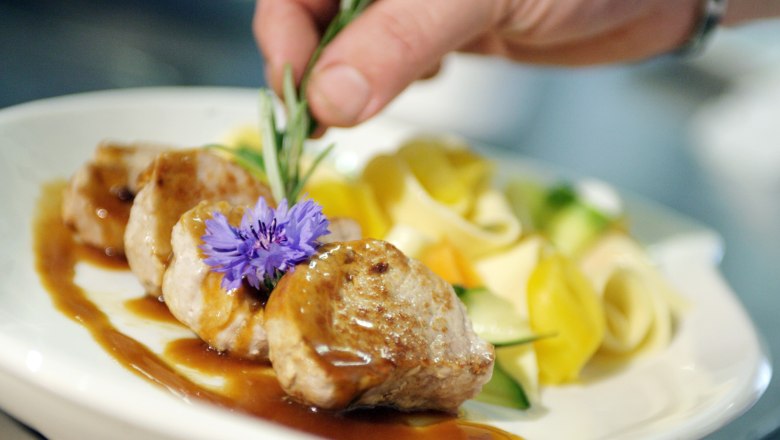 Gästehaus Bsteh, © Franz Weingartner Ein Teller mit Fleisch, Soße, Nudeln und Gemüse, dekoriert mit einer Blume und Rosmarin.