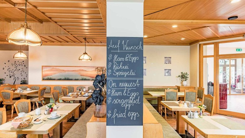 fruhstuck02, © Hotel Garni Steinfeld Frühstücksraum mit Holzmöbeln und einer Tafel mit Frühstücksoptionen.