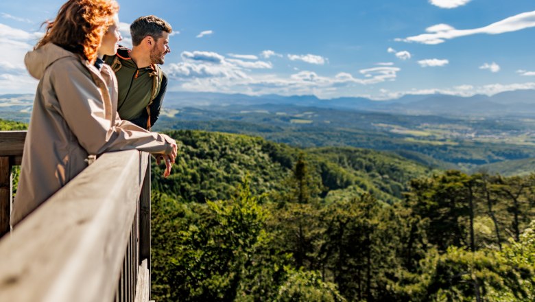 Auf der Plattform des Aussichtsturmes, © Wiener Alpen/Fülöp, Kremsl Zwei Personen stehen auf der Plattform des Aussichtsturmes Lanzenkirchen/Wiesen und blicken über eine bewaldete Landschaft mit Bergen im Hintergrund.