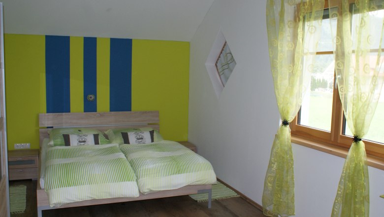 Schlafzimmer mit Doppelbett, © Familie Zwinz Schlafzimmer mit Doppelbett, grün-gelb gestreifte Wand, grüne Vorhänge, Holzboden.