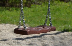 Spielplatz, © pixabay Eine leere Schaukel aus Holz und Metallketten hängt über einem Kiesboden, umgeben von grünem Gras.