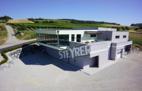 Weingut Steyrer, © Weingut Steyrer Modernes Weingut Steyrer mit Glasfassade und umliegenden Weinbergen.