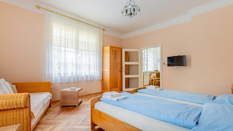 Schlafzimmer, © Wiener Alpen / Christian Kremsl Ein gemütliches Schlafzimmer mit zwei Einzelbetten, einem Sofa, einem Schrank und einem kleinen Tisch. Ein Fenster mit Vorhängen lässt Tageslicht herein.