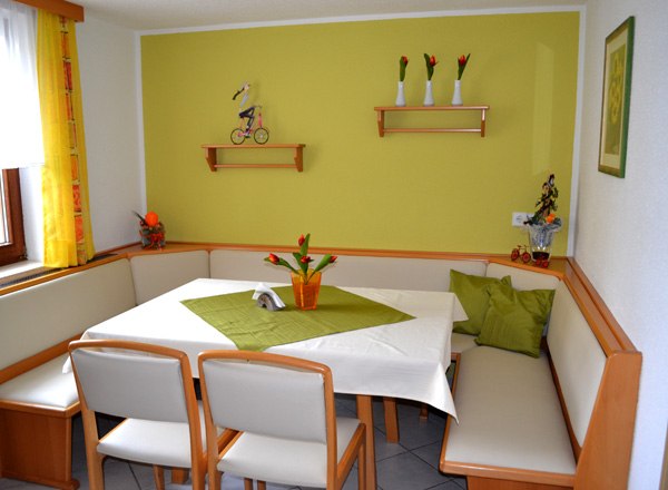 Sitzecke im Frühstücksraum, © Privatzimmer Leeb Gemütliche Sitzecke mit Eckbank und Tisch in einem Frühstücksraum, dekoriert mit grünen Akzenten und Blumen.
