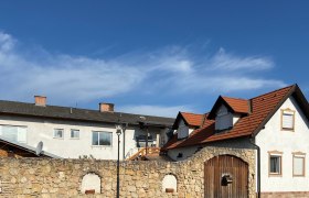 Ferienappartement Valenta, © Wiener Alpen Ein Gebäude mit roten Ziegeldächern und einer Steinmauer im Vordergrund unter blauem Himmel.